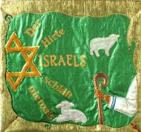 grünes Banner mit goldener Umrandung, orangem Davidstern, Arm mit Hirtenstab, 2 weißen Schafen und goldener Aufschrift 'Der Hirte Israels schläft niemals'
