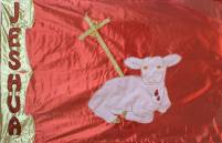 rote Flagge mit liegendem Lamm Gottes und Aufschrift 'JESHUA' auf goldenem Schaft